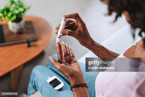 close-up of senior black woman pricking finger for glucose test at home - glucose stockfoto's en -beelden