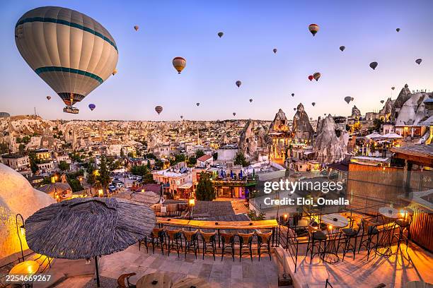des montgolfières créant une scène de voyage emblématique au-dessus du paysage unique de cheminées féeriques de goreme et illuminant les bâtiments villageois de la cappadoce, en turquie, à l’aube - cheminée de fée photos et images de collection