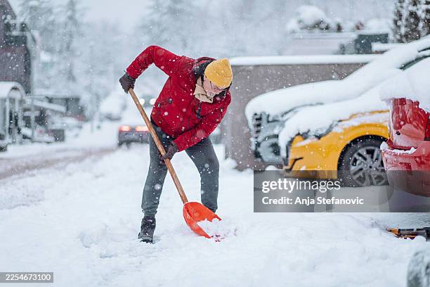 uomo con la giacca rossa che spalava la neve durante una forte nevicata in una zona residenziale - scavare foto e immagini stock