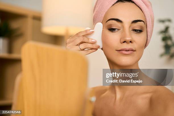 donna che si applica lo strumento gua sha sul viso - massaggio del viso foto e immagini stock