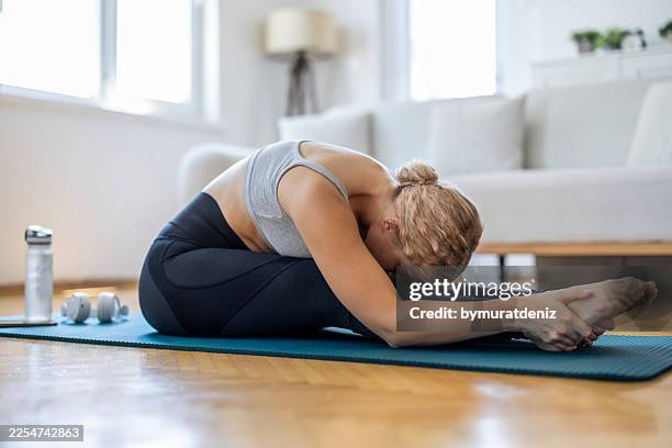joven realizando estiramientos de yoga sentada hacia adelante en casa para flexibilidad y relajación - encorvado fotografías e imágenes de stock