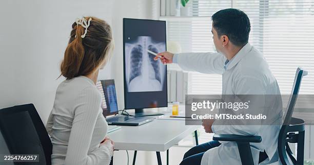 adult male doctor explaining lung x-ray results to young female patient during consultation in clinic office. medical health care concept. - symptom stock pictures, royalty-free photos & images
