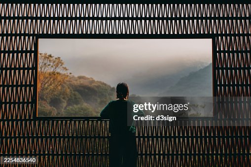 Rear view of young Asian woman enjoying the spectacular scenery during sunrise from a Chinese style balcony with traditional pattern and looking into the distance. Travel and vacation. Exploration and discovery concept Rear view of young Asian woman enjoying the spectacular scenery during sunrise from a Chinese style balcony with traditional pattern and looking into the distance. Travel and vacation. Exploration and discovery concept