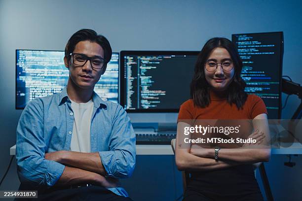 smiling tech team asian professionals confidently sit in front of computer with code on screen in office at night. portrait, working late, software developer, artificial intelligence and programming. - java code stock pictures, royalty-free photos & images