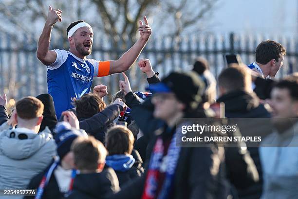 Macclesfield's English midfielder Paul Dawson is hoisted above the crowd as supporters storm the pitch to celebrate the team's victory at the end of...