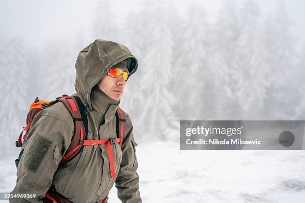 winter hiker in hooded jacket with red backpack trekking through snowy forest - long coat stock pictures, royalty-free photos & images