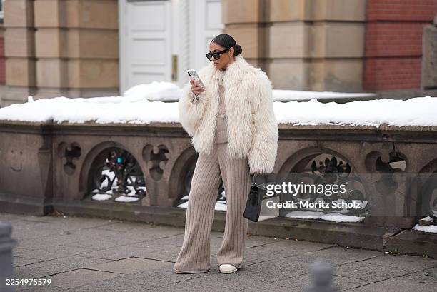 Cherifa is seen wearing a cream colored shearling jacket with a voluminous oversized silhouette, long textured fur and dropped shoulders from Ducie...