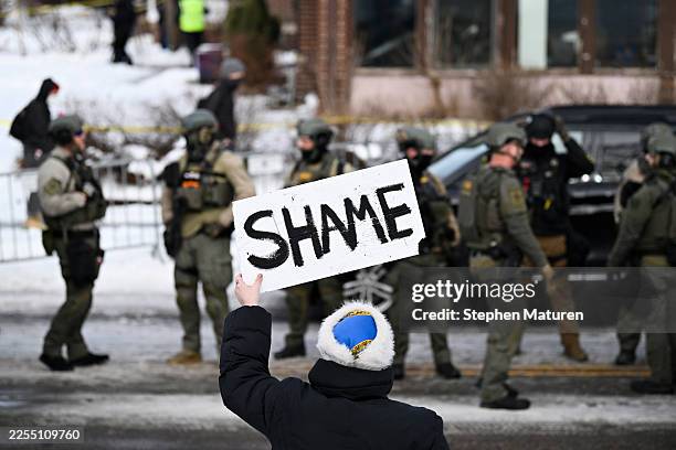 An onlooker holds a sign that reads "Shame" as members of law enforcement work the scene following a suspected shooting by an ICE agent during...