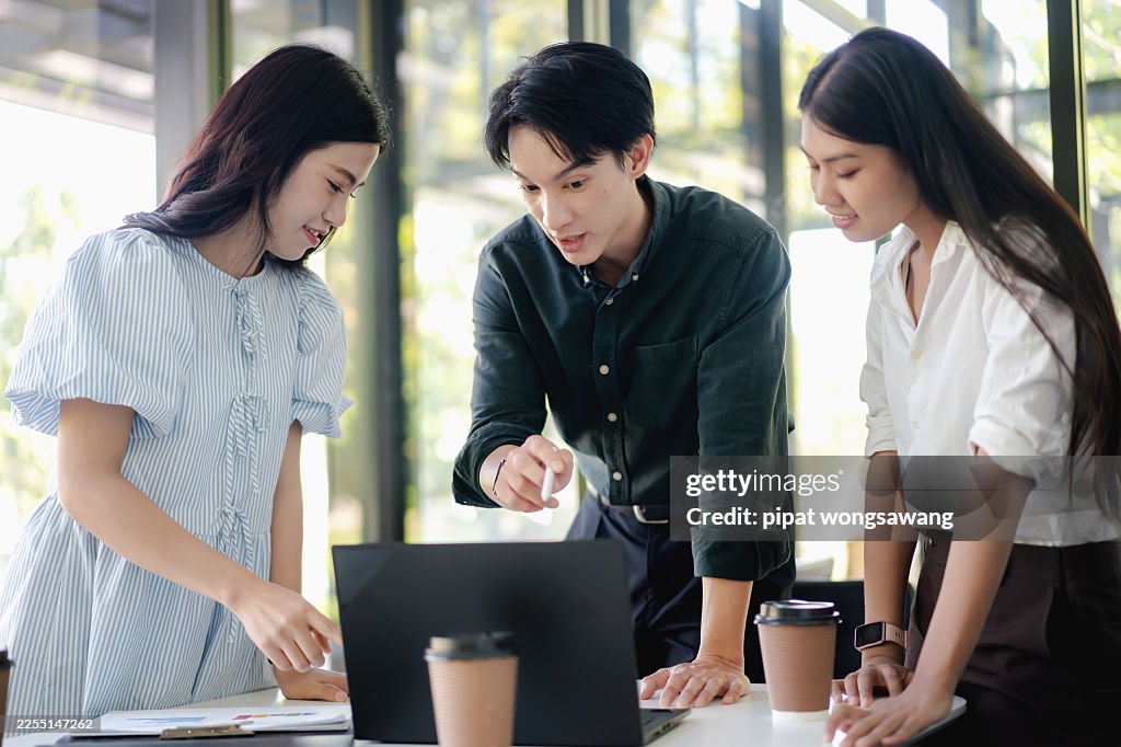 Asian coworkers brainstorming ideas around laptop in modern office