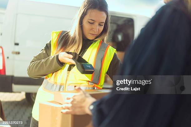 female delivery worker scanning a barcode on a parcel using a handheld scanner device during a customer drop-off - agenda eletrónica imagens e fotografias de stock