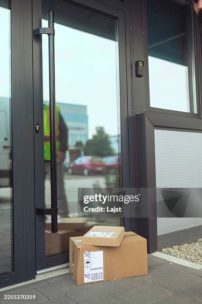 cardboard parcels delivered at the front door of a modern office or house, with a courier reflected in the glass - contactless delivery stock pictures, royalty-free photos & images