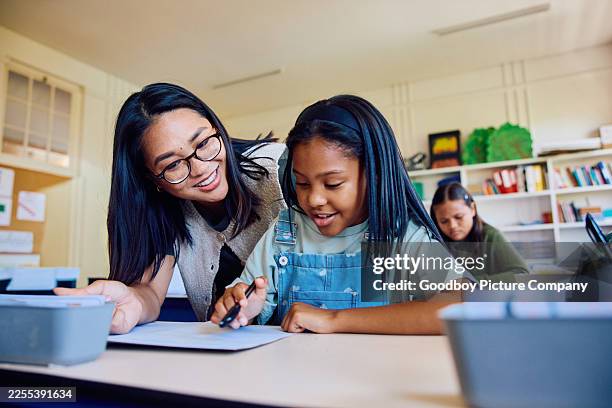 cheerful elementary teacher and student working together on writing task at desk in classroom - study guide stock pictures, royalty-free photos & images