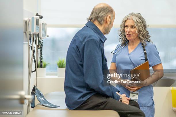 compassionate nurse discussing patient health with elderly gentleman in clinic - phonendoscope stock pictures, royalty-free photos & images