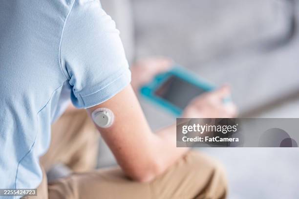 casual person in light blue shirt with arm wearable sensor using handheld device - type 1 diabetes stock pictures, royalty-free photos & images