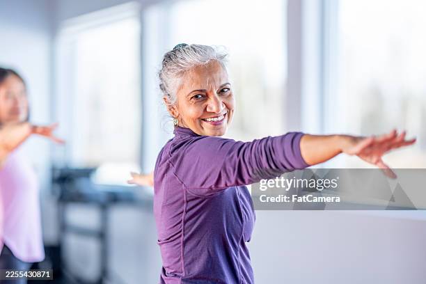 donna senior sorridente in abbigliamento sportivo viola dimostra equilibrio ed esercizio in classe - anziani attivi foto e immagini stock