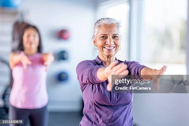 confident senior woman leads fitness class with arm stretches in bright studio - boa postura imagens e fotografias de stock