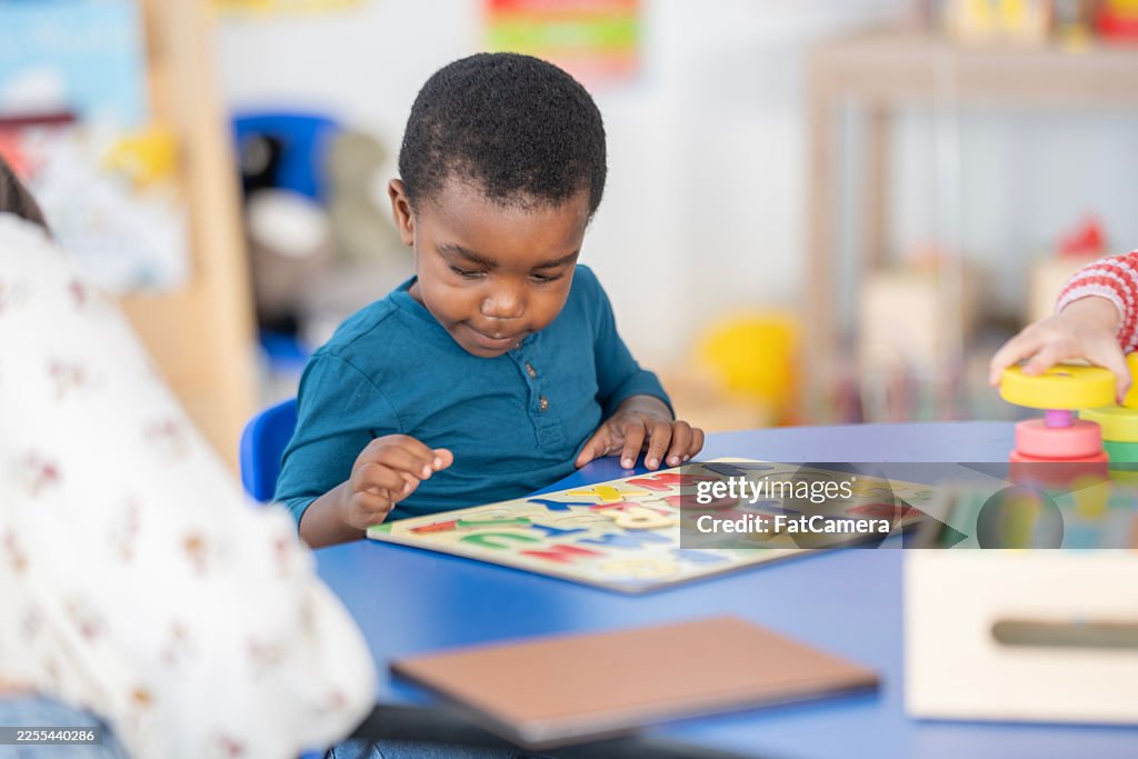 Child Engaged In Colorful Puzzle At Table In Bright Classroom Setting