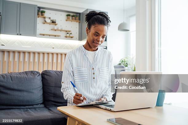 latina investor working remotely from home on laptop in modern apartment - afro caribbean people stock pictures, royalty-free photos & images