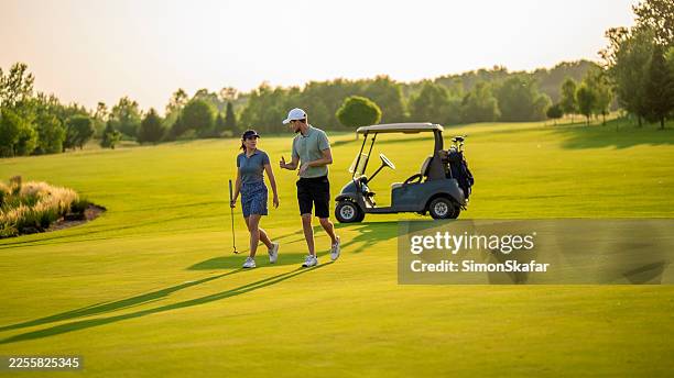couple walking on golf course with cart in background - golf cart stock pictures, royalty-free photos & images