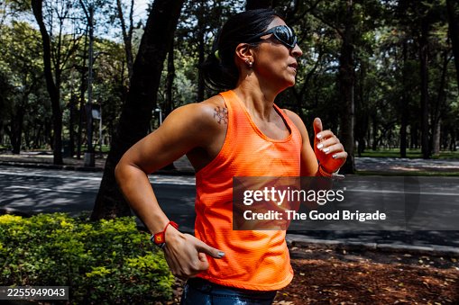 Determined female runner training under shade in park Determined female runner training under shade in park