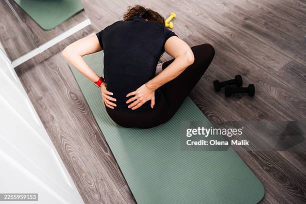 woman sitting on fitness mat feeling back pain after home workout - lower back stock pictures, royalty-free photos & images