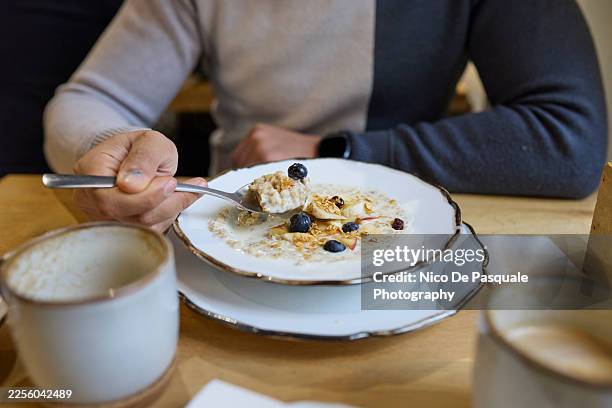 man eating oat pudding with apple blueberries and nuts at café table, poland - oatmeal stock pictures, royalty-free photos & images