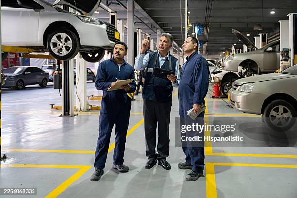 team of mechanics looking under a car at a garage while holding a tablet - machine part stock pictures, royalty-free photos & images