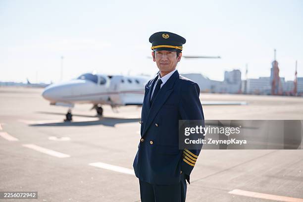professional male pilot standing on airport runway in front of private jet - aviation hat stock pictures, royalty-free photos & images