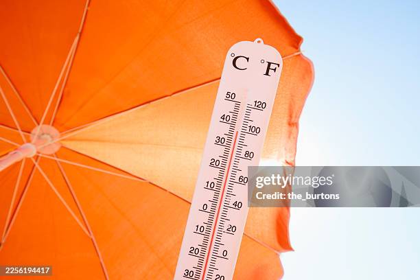thermometer against orange parasol, sky and sun - thermomètre photos et images de collection