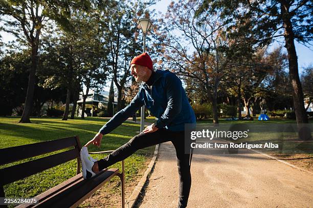 mature adult man stretching while exercising in park - park bench stock pictures, royalty-free photos & images