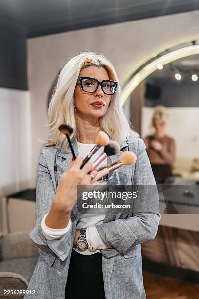mittelerwachsene weibliche kosmetikerin hält make-up-pinsel in einem schönheitssalon - permanent make up stock-fotos und bilder