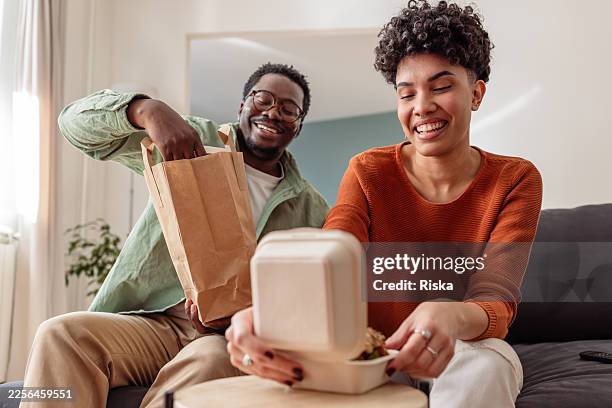 man and woman enjoying takeout at home, sharing laughter while opening food boxes - contactless delivery stock pictures, royalty-free photos & images