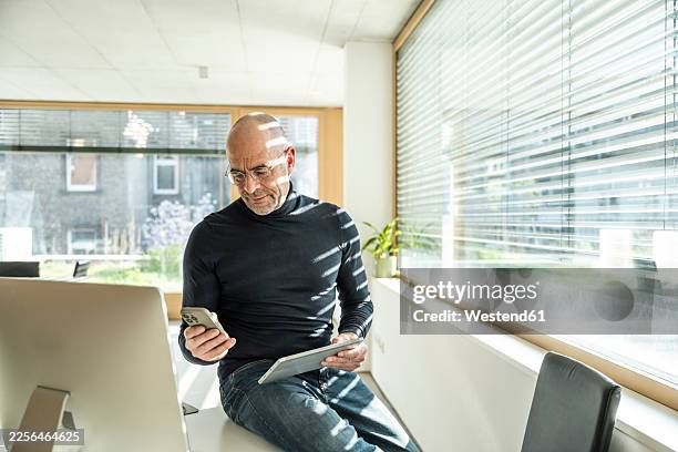 businessman in office using smartphone and tablet with concentration - receding hairline stock pictures, royalty-free photos & images