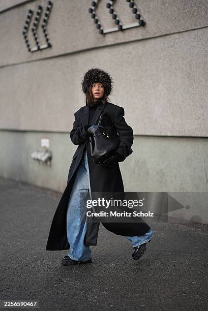 Sophia Geiss is seen wearing a long black tailored wool coat with a straight silhouette and lapel collar from Herskind; a black knit sweater with a...