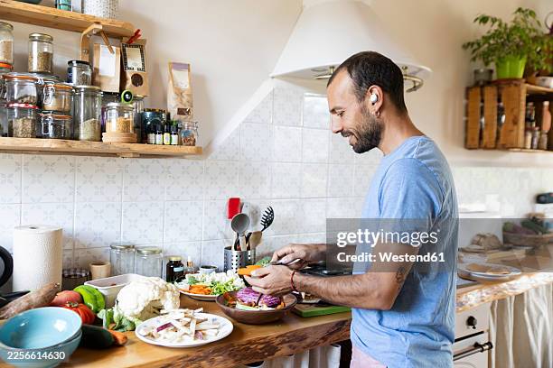 smiling man preparing fresh vegetables in home kitchen - balancing plates stock pictures, royalty-free photos & images