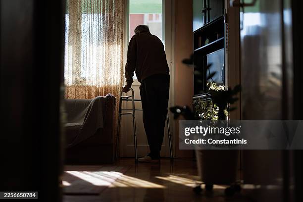 elderly man with walker looking out window, contemplating life in quiet solitude - solitude stock pictures, royalty-free photos & images