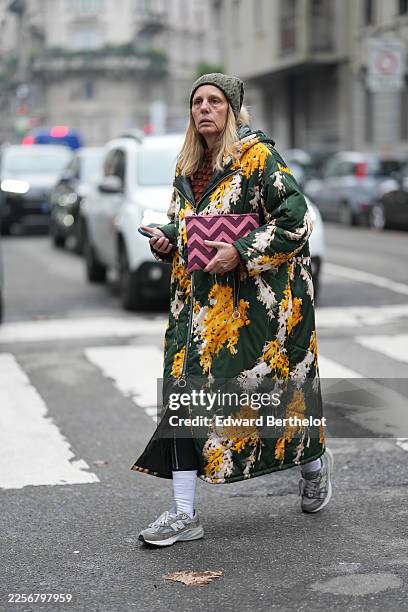 Guest wears straight shoulder-length blonde hair with a middle part, a pink and magenta chevron clutch bag, an olive green knit beanie, a brown...