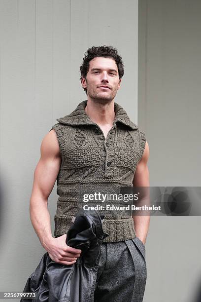 Guest wears short curly dark brown hair, olive green cable-knit sleeveless pullover with a folded polo-style collar and three-button placket, black...