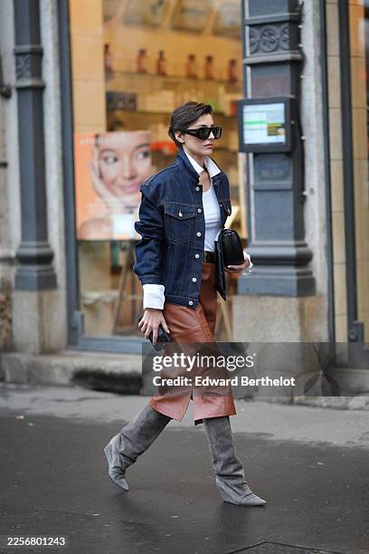 Guest wears short dark pixie haircut with a side part, oversized black rectangular sunglasses, black leather clutch bag handheld, dark blue indigo...