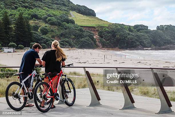 Cyclists stop to look at a landslide while a search is underway by local emergency services for missing people at Mount Maunganui in Tauranga on...