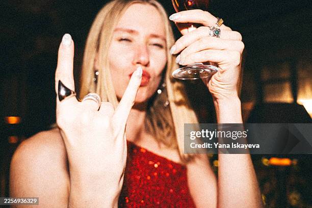 party moment: toasting with a glass while flashing a rock gesture in a lively celebration, capturing bold confidence, friendship, and self-expression in a festive nightlife scene. film photo - high self esteem stock pictures, royalty-free photos & images
