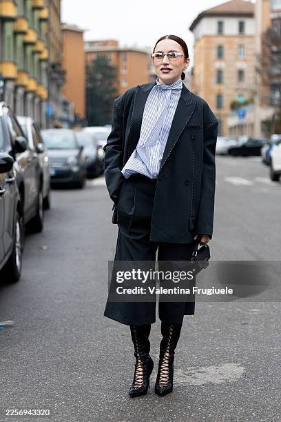 Gergana Lazarova wears an oversized black tailored coat over a blue-and-white striped blouse with bow tie detail, cropped black trousers, black...