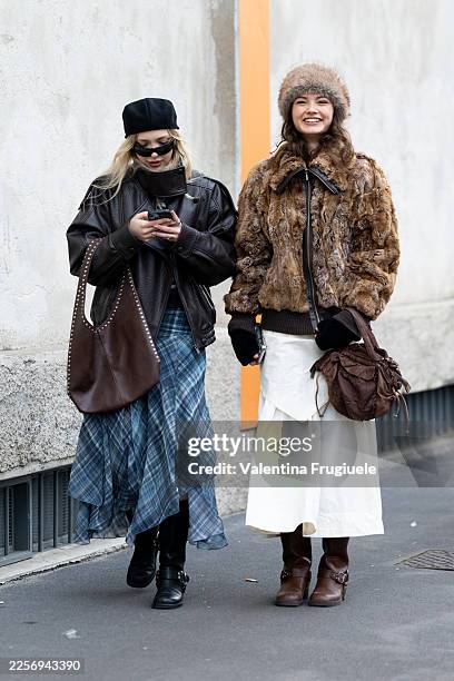 Guest wears a brown oversized leather jacket over a blue plaid asymmetric skirt, paired with black ankle boots and carrying a large brown studded...