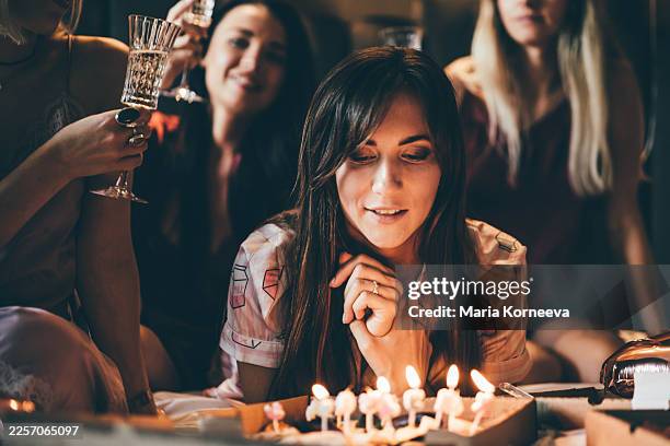 a young woman makes a wish while looking at birthday candles, surrounded by friends in a dimly lit room. this intimate, warm scene captures the essence of hope, personal milestones, and the beauty of shared celebrations. - desiderio foto e immagini stock