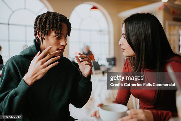 a young, enthused man gestures while explaining something as a woman listens at a café table. - leidenschaft stock-fotos und bilder