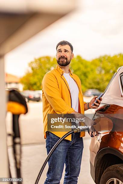 hombre repostando su coche en una gasolinera durante el día con una bomba de combustible en la mano - diésel tipo de combustible fotografías e imágenes de stock