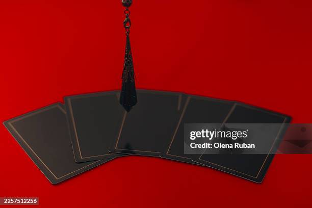 five black cards are fanned out on a red surface with a dark pendulum hanging above them. - face down cards stock pictures, royalty-free photos & images