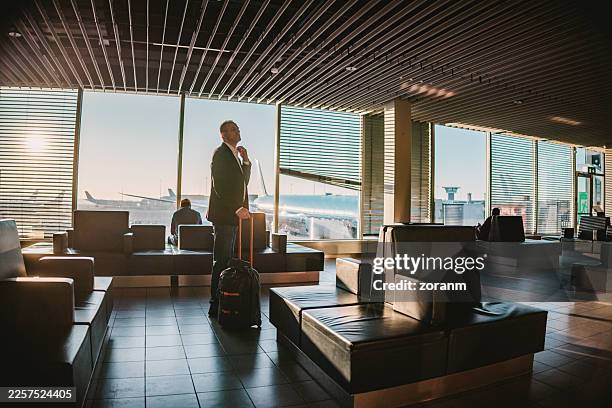 empresario de mediana edad con equipaje con ruedas de pie en la sala del aeropuerto vacía - sala de embarque del aeropuerto fotografías e imágenes de stock