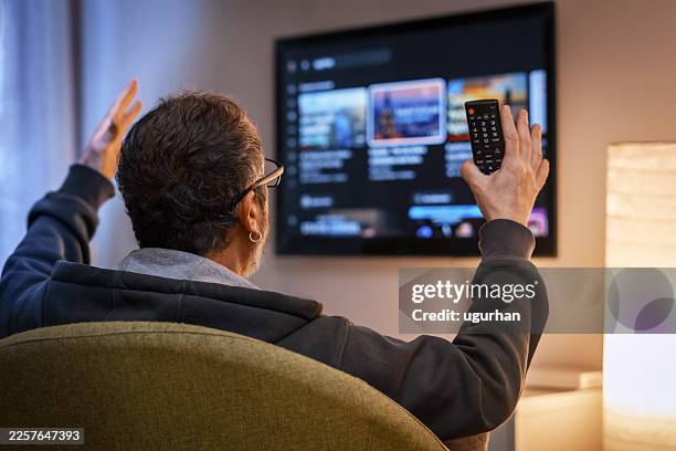 hombre navegando contenido en streaming en smart tv con mando a distancia - smart tv fotografías e imágenes de stock