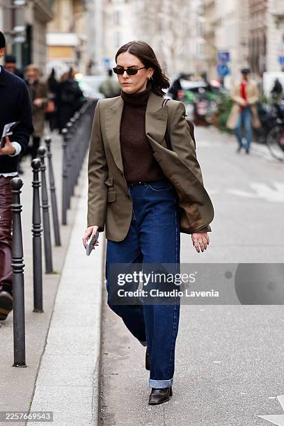Guest wears brown turtleneck sweater, blue wide leg jeans, olive green blazer, outside Issey Miyake, during the Menswear Fall/Winter 2026-2027 as...